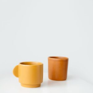Bright yellow and orange ceramic cups placed on table against white background in daylight